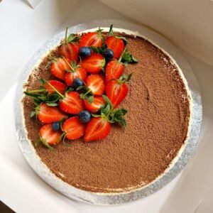 Top view of a tiramisu cake decorated with fresh strawberries and blueberries, perfect for dessert lovers.