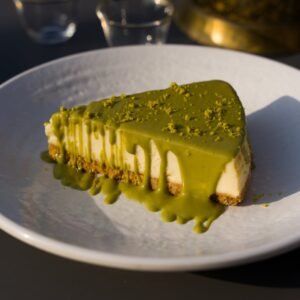 A close-up of a creamy cheesecake slice drizzled with rich matcha glaze on a white plate.