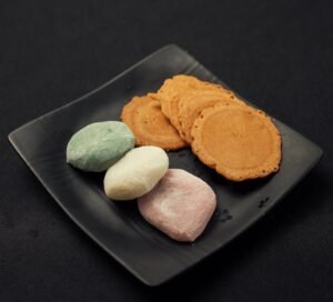 Colorful mochi and cookies arranged elegantly on a black plate.
