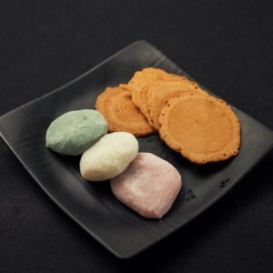 Colorful mochi and cookies arranged elegantly on a black plate.