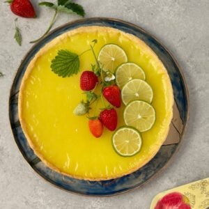 Top view of a citrus tart garnished with lime and strawberries on a light surface.